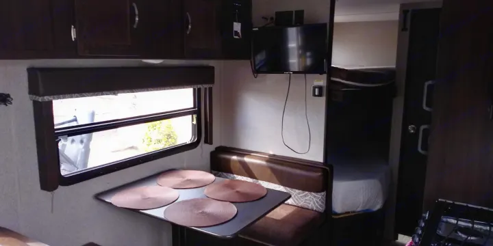 RV rental interior featuring a cozy dinette, window view, mounted TV, and a glimpse into a sleeping bunk area.. Keystone RV Springdale 2018