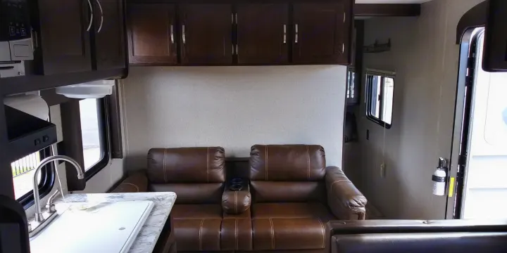This RV rental features a modern interior with dark wood cabinets, a kitchen sink, microwave, and comfy brown leather recliners.. Keystone RV Springdale 2018
