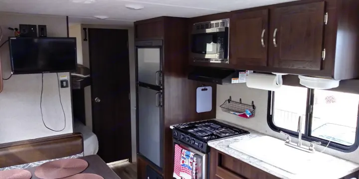 RV rental interior: a well-equipped compact kitchen with stove, microwave, fridge, sink, plus a dining area and TV.. Keystone RV Springdale 2018