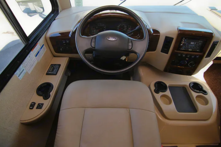 Interior view of an RV rental's driver cockpit, highlighting the Ford steering wheel, dashboard with infotainment, and essential controls.. Thor Hurricane 2018