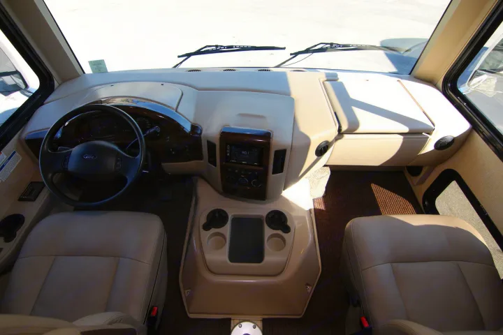 Tan RV rental interior cockpit with steering wheel, dashboard, center console, and two front seats.. Thor Hurricane 2018