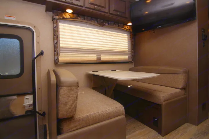 Cozy RV rental dinette with window, overhead cabinets, and TV. Ideal for meals in your travel trailer.. Thor Hurricane 2018