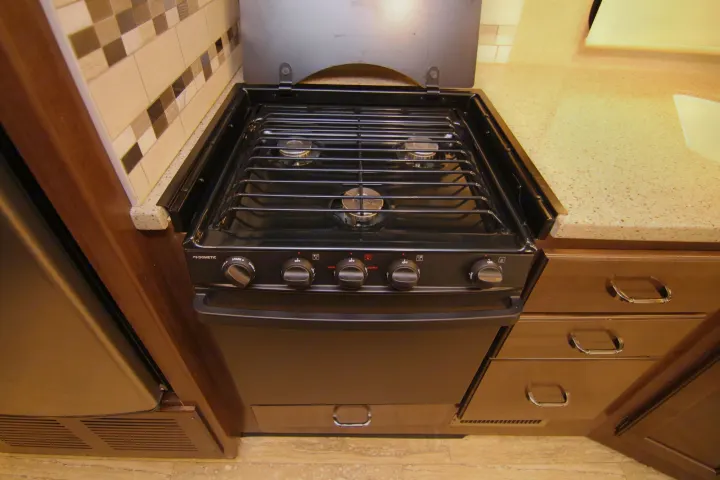 RV rental kitchen featuring a black Dometic stove and oven, speckled countertop, and patterned backsplash. Perfect for cooking.. Thor Hurricane 2018