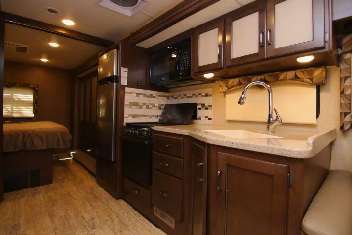 Functional RV rental interior featuring a fully equipped kitchen (sink, stove, microwave, fridge) and a cozy bedroom.. Thor Hurricane 2018