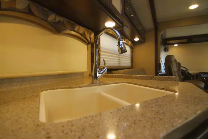 Modern RV rental kitchen featuring a double sink, chrome faucet, and speckled countertop under cabinet lights.. Thor Hurricane 2018