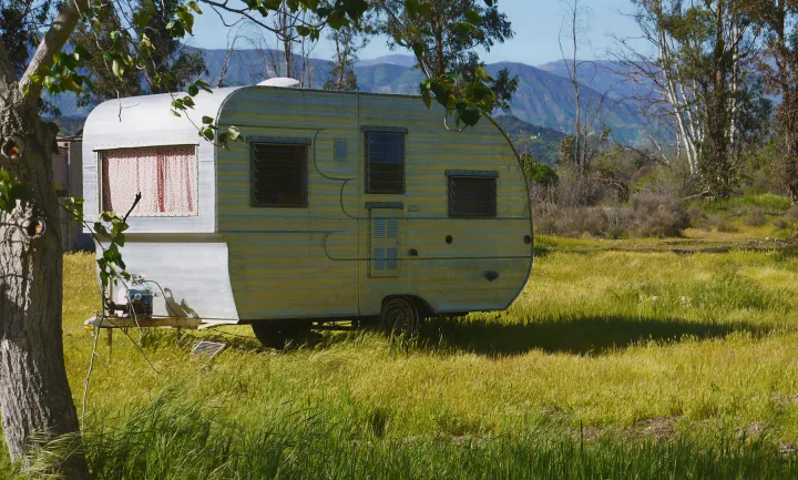 Rustic RV rental parked in a sun-drenched field with distant mountains. An ideal vintage travel trailer for peaceful escapes.. Shasta Oasis 1959