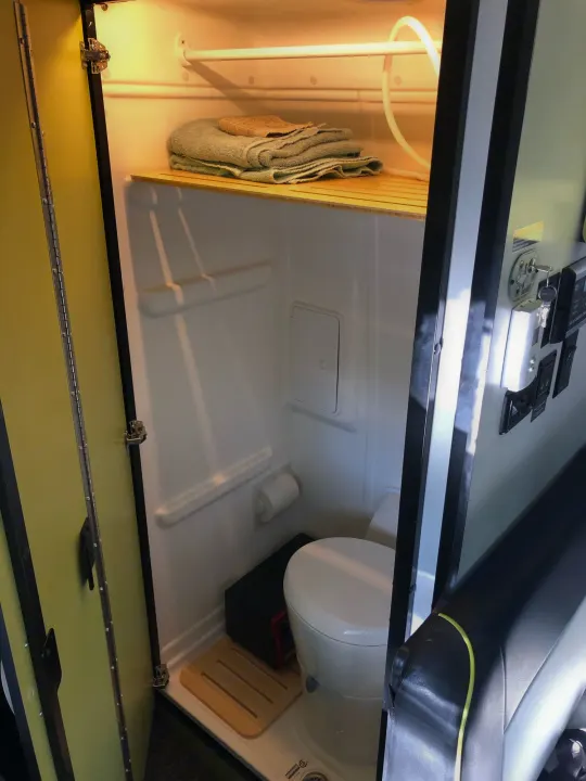 Compact RV rental wet bath featuring a toilet, shower, and shelf with towels. Ideal for comfortable road trips.. Winnebago Mercedes Sprinter 2019