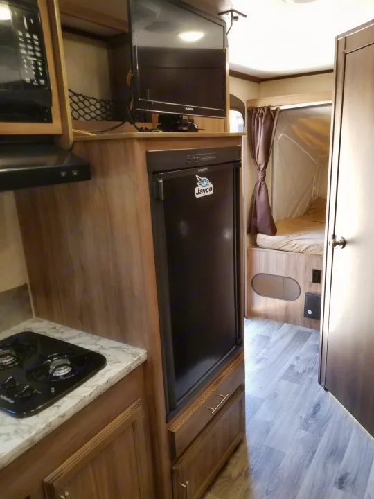 Inside this RV rental: compact kitchen with stove, microwave, fridge, TV, and a comfy pop-out bed. Ideal for road trips!. Jayco Jay Feather 2018