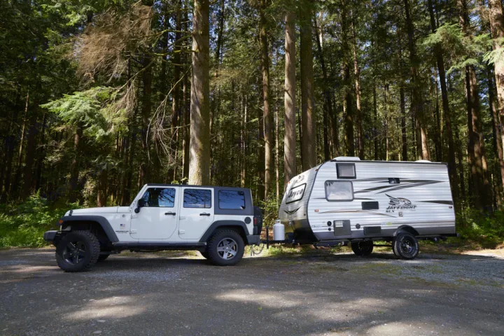 Experience nature! This RV rental includes a white Jeep towing a Jayco travel trailer, parked in a lush forest campsite.. Jayco Baja 154BH 2016