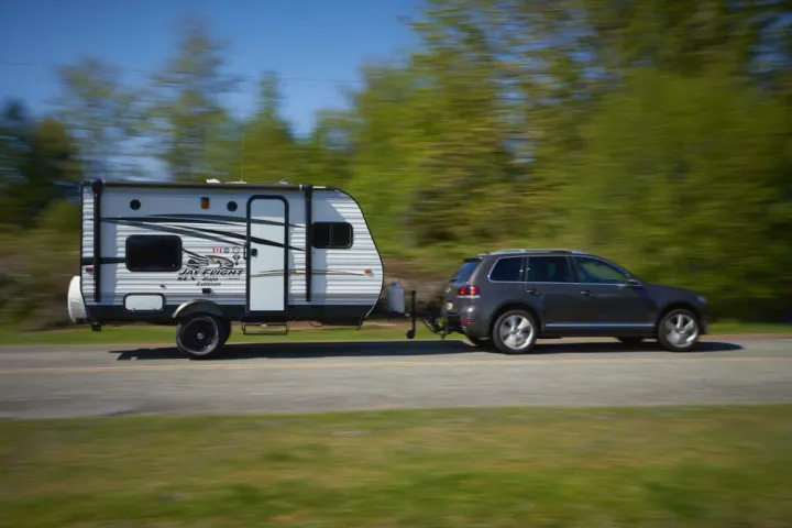 An SUV towing a white Jay Flight travel trailer (RV rental) on a road, with blurred green trees, indicating motion.. Jayco Baja 154BH 2016