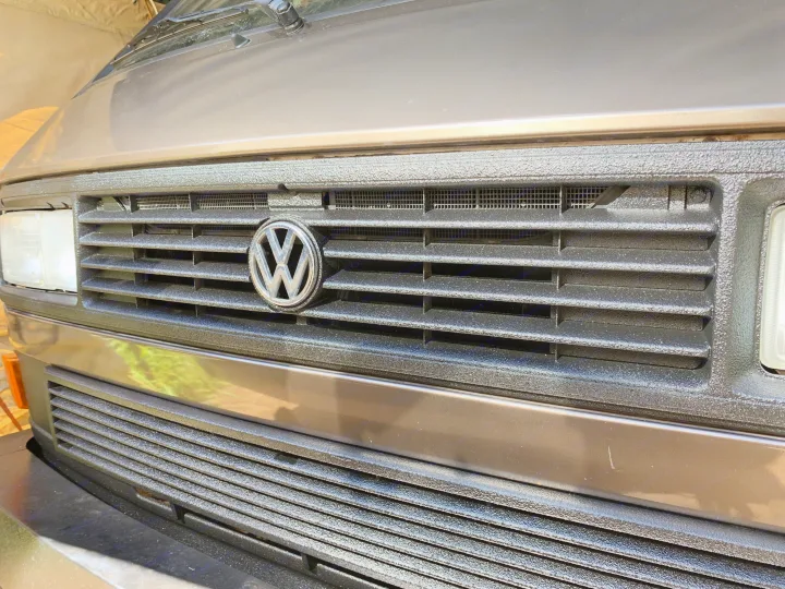 Brown VW van's front with textured black grille, prominent VW emblem, and clear headlights. Great for RV rental!. VW Westfalia 1986