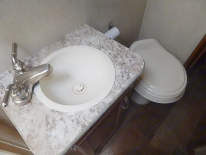 Compact RV rental bathroom featuring a sink with a brushed nickel faucet, a marbled counter, and a toilet.. Gulf Stream Conquest 2016