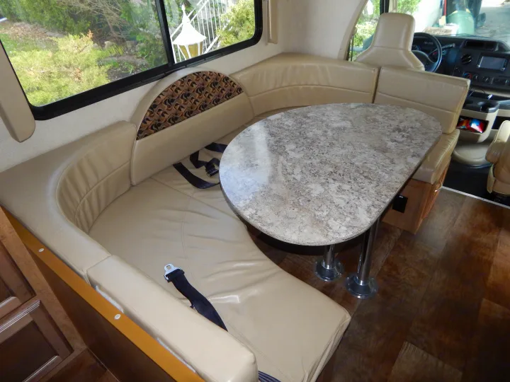 RV rental's inviting interior: a U-shaped dinette with a speckled table and plush seating, visible cockpit in background.. Gulf Stream Conquest 2016