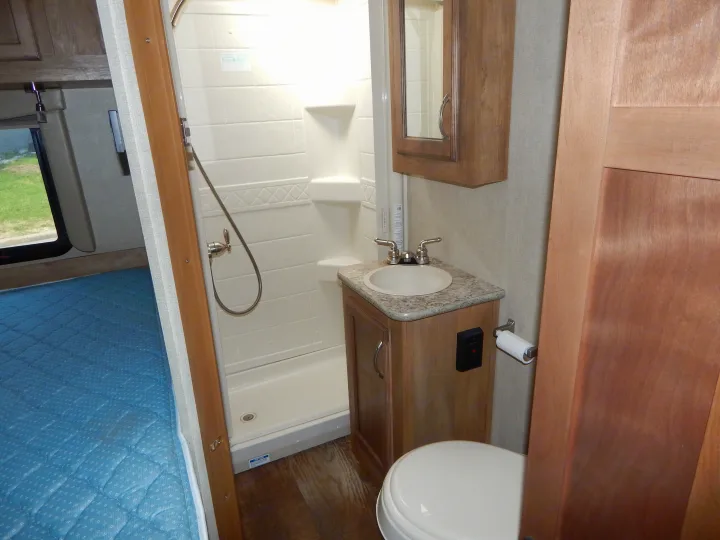 RV rental interior: practical bathroom with shower, sink, and toilet, next to a cozy bedroom setup.. Gulf Stream Conquest 2016