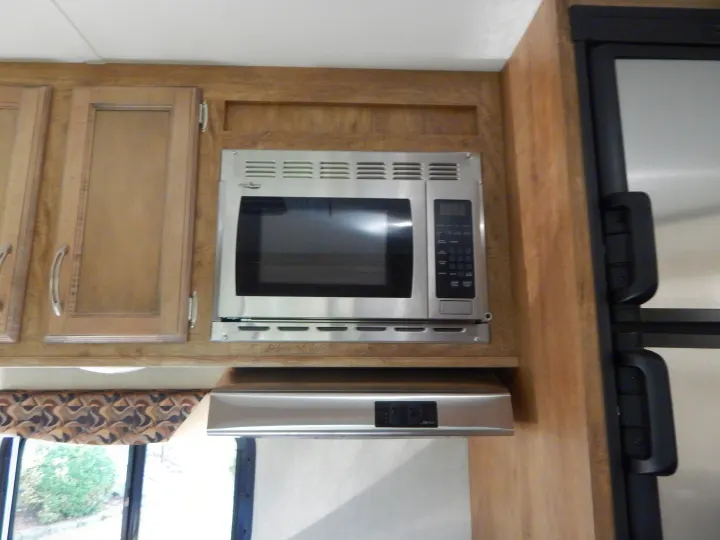 RV rental kitchen: Stainless microwave, range hood, wooden cabinets, and fridge.. Gulf Stream Conquest 2016