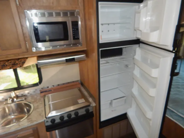 Inside an RV rental: a compact kitchen with microwave, sink, stove, and an open refrigerator showing ample storage.. Gulf Stream Conquest 2016