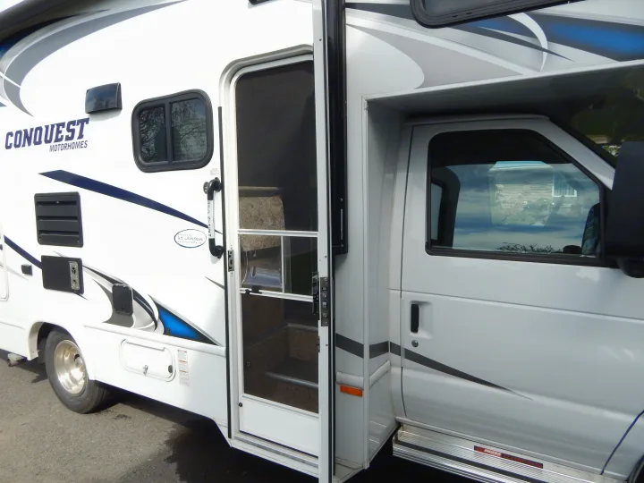 White Conquest motorhome RV rental, with its main door open showing interior steps and blue side graphics.. Gulf Stream Conquest 2016