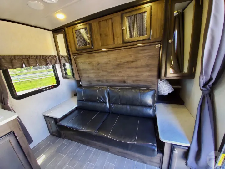 Experience comfort in this **RV rental**! Features a black faux-leather couch, convertible bed, wood cabinets, and window.. Heartland Wilderness 2020