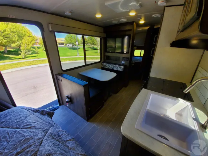 This RV rental interior features a cozy bed, dinette, kitchen with sink, and large windows revealing a scenic outdoor view.. Heartland Wilderness 2020