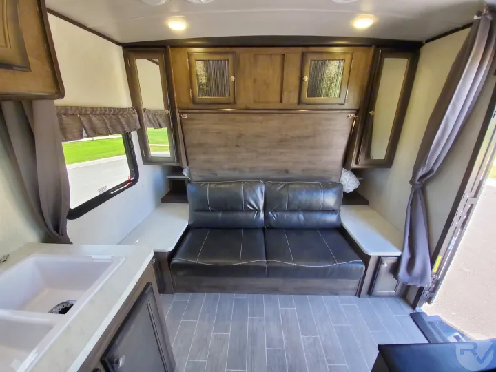 RV rental interior: compact space with a black sofa, overhead cabinets, sink, and wood-look flooring.. Heartland Wilderness 2020