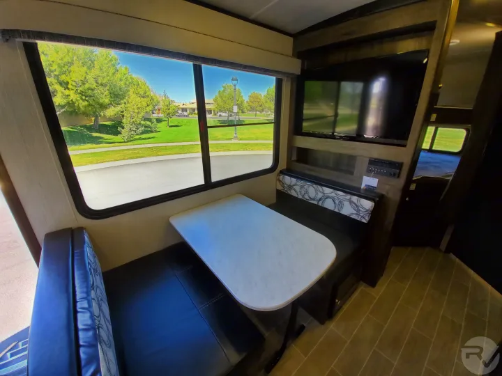 Spacious RV rental dinette with scenic window view of trees & street, TV, and comfortable seating. Ideal for cozy trips.. Heartland Wilderness 2020