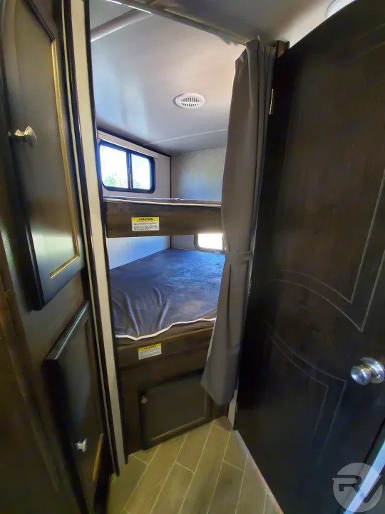 Inside this RV rental, a compact bunk bed sleeping area features two beds, windows, a ceiling vent, and a privacy curtain.. Heartland Wilderness 2020