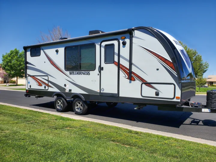 A sleek white RV travel trailer with bold black & brown graphics, parked on a sunny street. Perfect for your next rv rental!. Heartland Wilderness 2020
