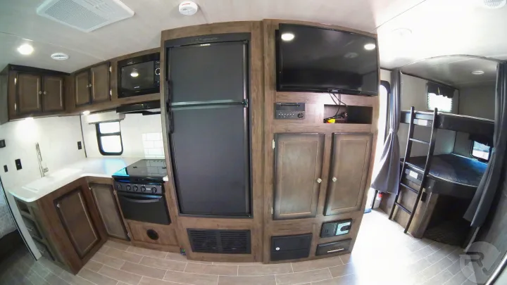 Spacious rv rental interior featuring a modern kitchen with appliances, a large refrigerator, TV area, and comfy bunk beds.. Heartland Wilderness 2020