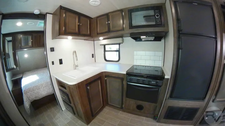 Explore this modern RV rental kitchen featuring a stove, microwave, fridge, and sink, showcasing compact living and bedroom access.. Heartland Wilderness 2020