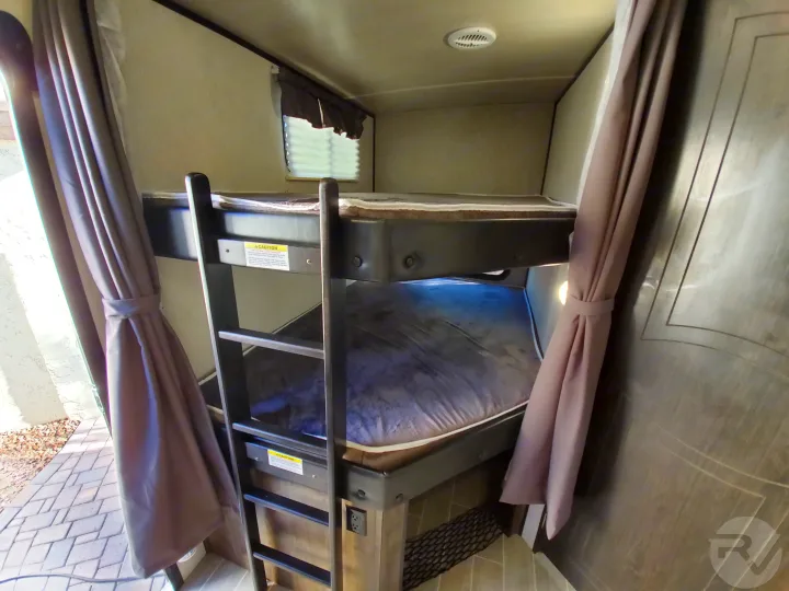 Inside an RV rental: cozy bunk beds with a ladder, window, and privacy curtains, offering comfortable extra sleeping space.. Heartland Wilderness 2020