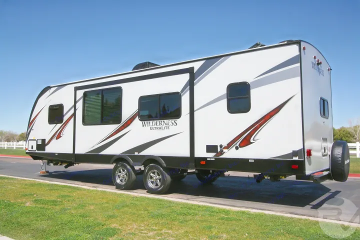 A white Wilderness Ultralite travel trailer, perfect for an RV rental or camping trip, parked under a clear sky.. Heartland Wilderness 2020