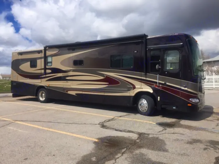 This beautiful brown & tan luxury motorhome, perfect for an RV rental adventure, is parked on asphalt under a cloudy sky.. Damon Tuscany 2008
