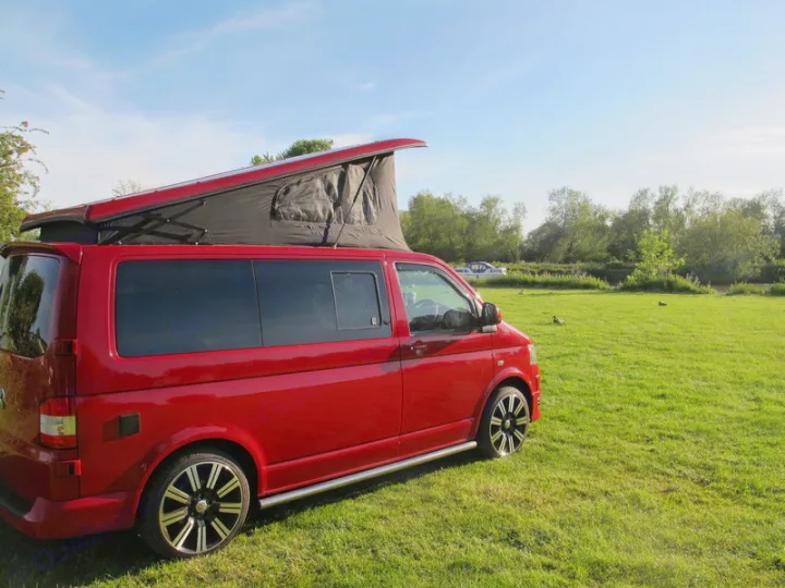Red pop-top VW camper, perfect for rv rental adventures, parked on a sunny grassy field with ducks nearby.. Volkswagen T5 premium camper 2011