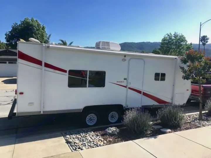 A white RV rental travel trailer, branded 'Mavric' with red and grey stripes, parked on a sunny street.. Eclipse Recreational Vehicles Maveric 2011
