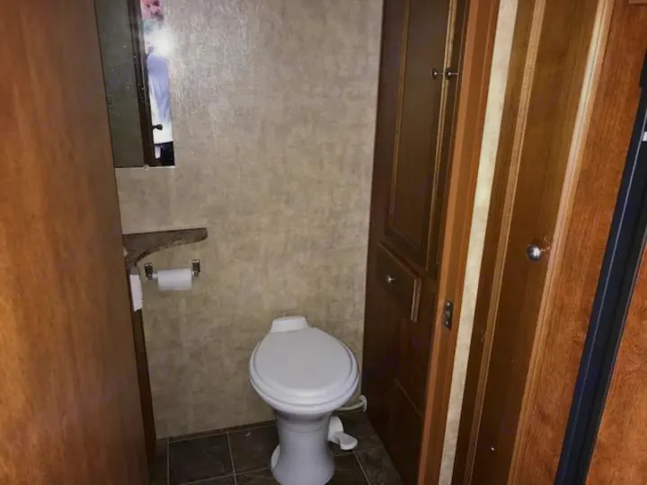 RV rental bathroom with a white toilet, wood cabinets, and mirror reflection. Compact and functional RV interior.. Eclipse Recreational Vehicles Maveric 2011