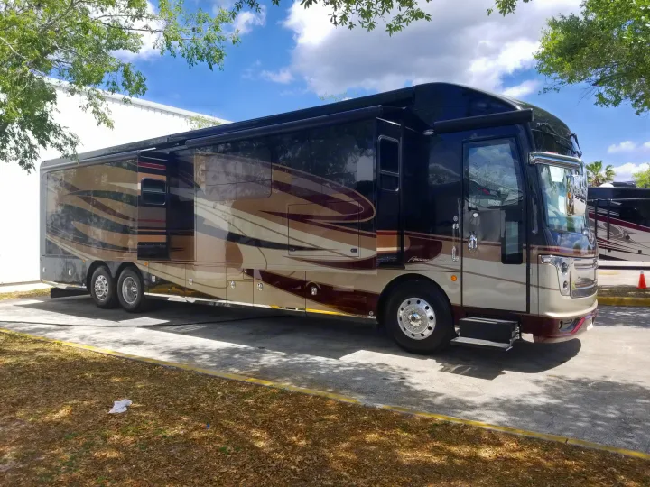 A large, luxurious American Coach RV, dark and tan with intricate design, parked outdoors. Ideal for rv rental adventures.. Fleetwood American Eagle 2019