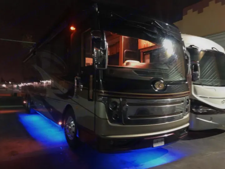 A dark luxury RV rental glows with vibrant blue underglow lights at night, showcasing its sleek design.. Fleetwood American Eagle 2019