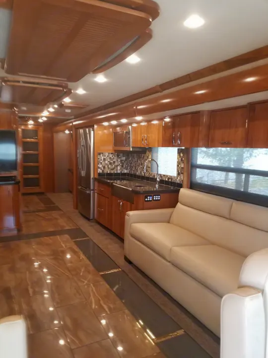 Luxurious RV rental interior: a sleek kitchen with stainless appliances, cream sofa, and elegant tiled floors.. Fleetwood American Eagle 2019