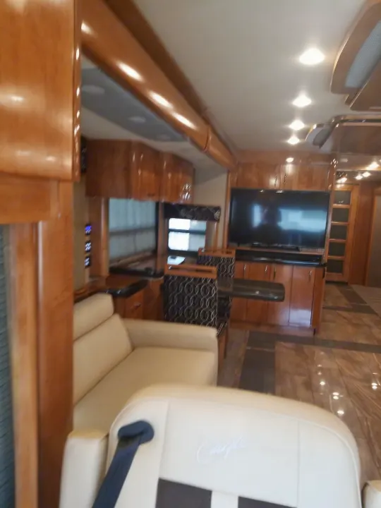 Inside this luxury RV rental: comfortable living space with light sofa, TV, dining area, and warm wood accents.. Fleetwood American Eagle 2019