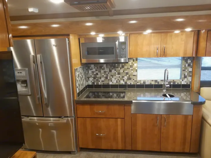 RV rental kitchen: modern design with stainless steel fridge, microwave, sink, cooktop, and wood cabinetry.. Fleetwood American Eagle 2019
