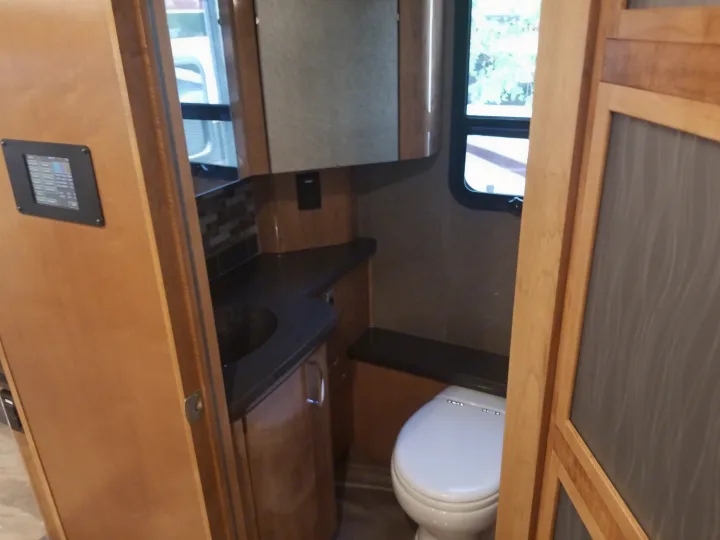 This RV rental bathroom features a modern sink, toilet, and a control panel on the left, offering a compact and functional space.. Fleetwood American Eagle 2019