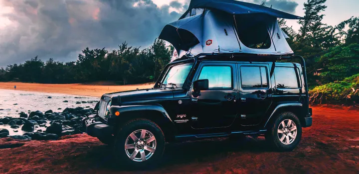 A black Jeep Wrangler, equipped with a rooftop tent, is parked on a scenic beach, offering a unique RV rental experience.. Jeep Wrangler Unlimited 2016