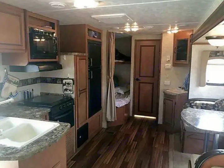 This RV rental interior shows a compact kitchen with microwave, fridge, stove, dining booth, and hallway to sleeping space.. Gulf Stream Conquest 2014