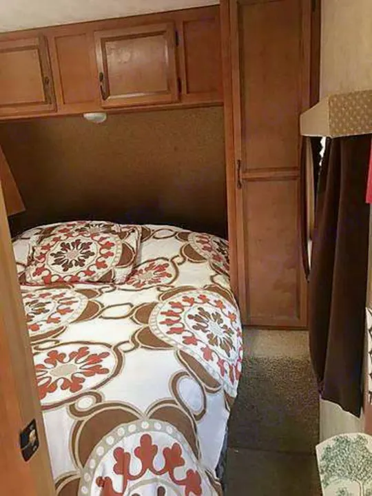 RV rental interior: A compact bedroom features patterned bedding, overhead cabinets, and a wardrobe.. Gulf Stream Conquest 2014