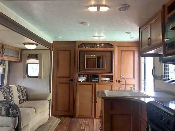 Inside a comfy RV rental: compact kitchen with sink & stove, plus a plush living area with sofa & cabinets.. Gulf Stream Conquest 2014