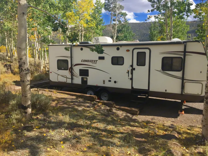 An RV rental, a white Conquest travel trailer, parked among golden Aspens in a scenic autumn campsite in the mountains.. Gulf Stream Conquest 2014