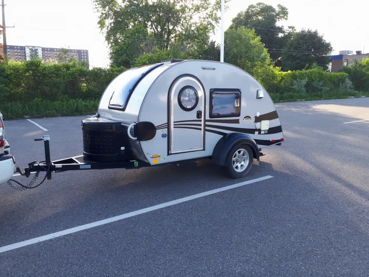 Grey teardrop camper RV rental, attached to a vehicle in a sunny parking lot.. Little Guy Silver Shadow 2016