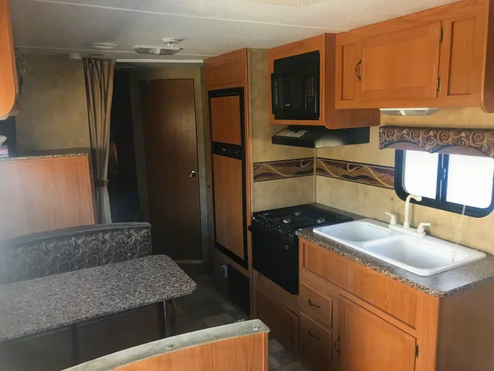 Experience comfort in this RV rental's interior, showcasing a complete kitchen with microwave, stove, sink, and dining booth.. Keystone Hideout 2009