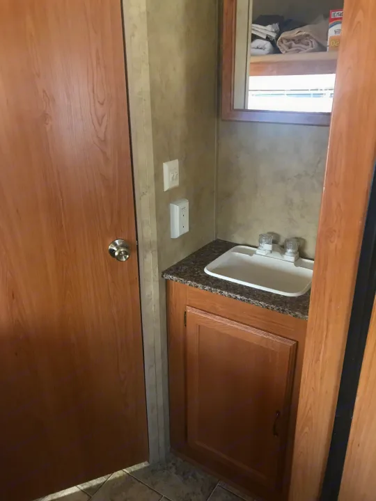 RV rental interior: A compact bathroom with a wooden door, sink, and mirrored cabinet above.. Keystone Hideout 2009