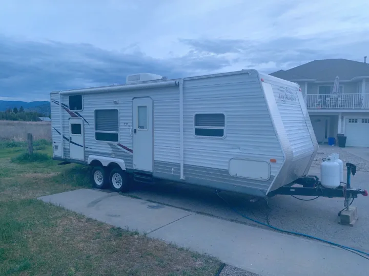 White Jay Flight travel trailer RV on concrete with propane tanks. Parked near a house & mountains, available for RV rental.. Jayco Jay Flight 2007